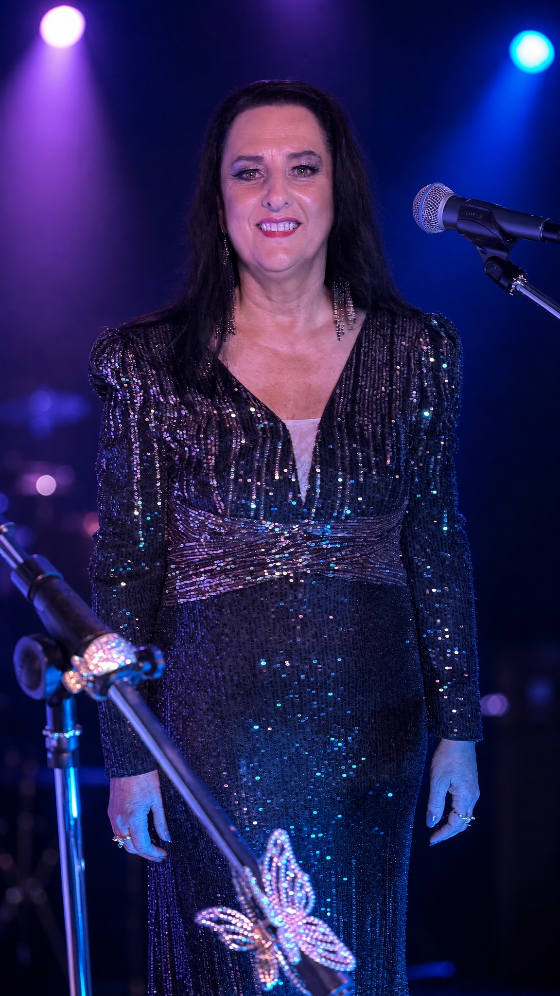Jannine Douglas on stage in a sparkling sequin gown under blue and purple stage lighting during a live performance