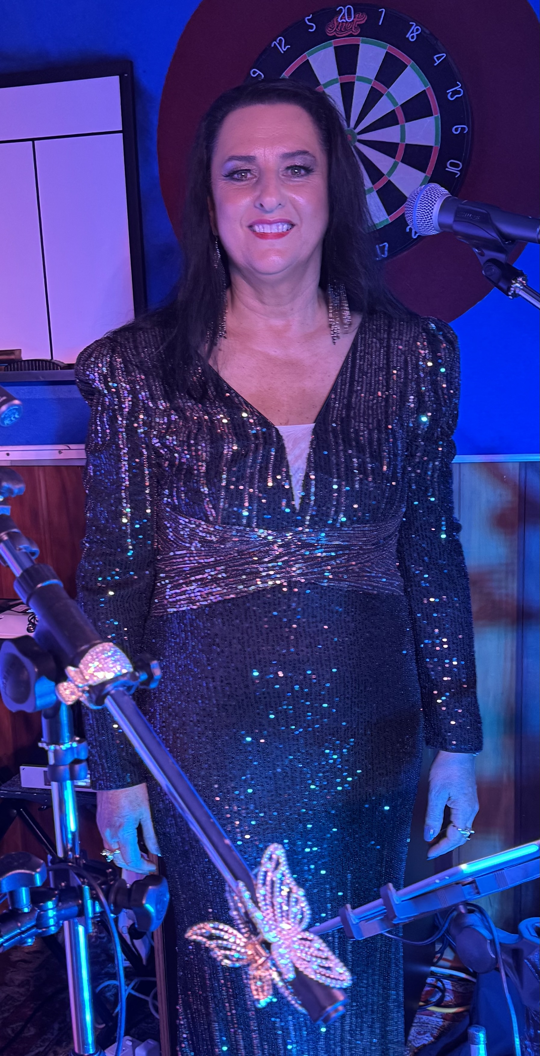 Jannine Douglas on stage in a sparkling butterfly-detail gown with blue stage lighting at a venue performance