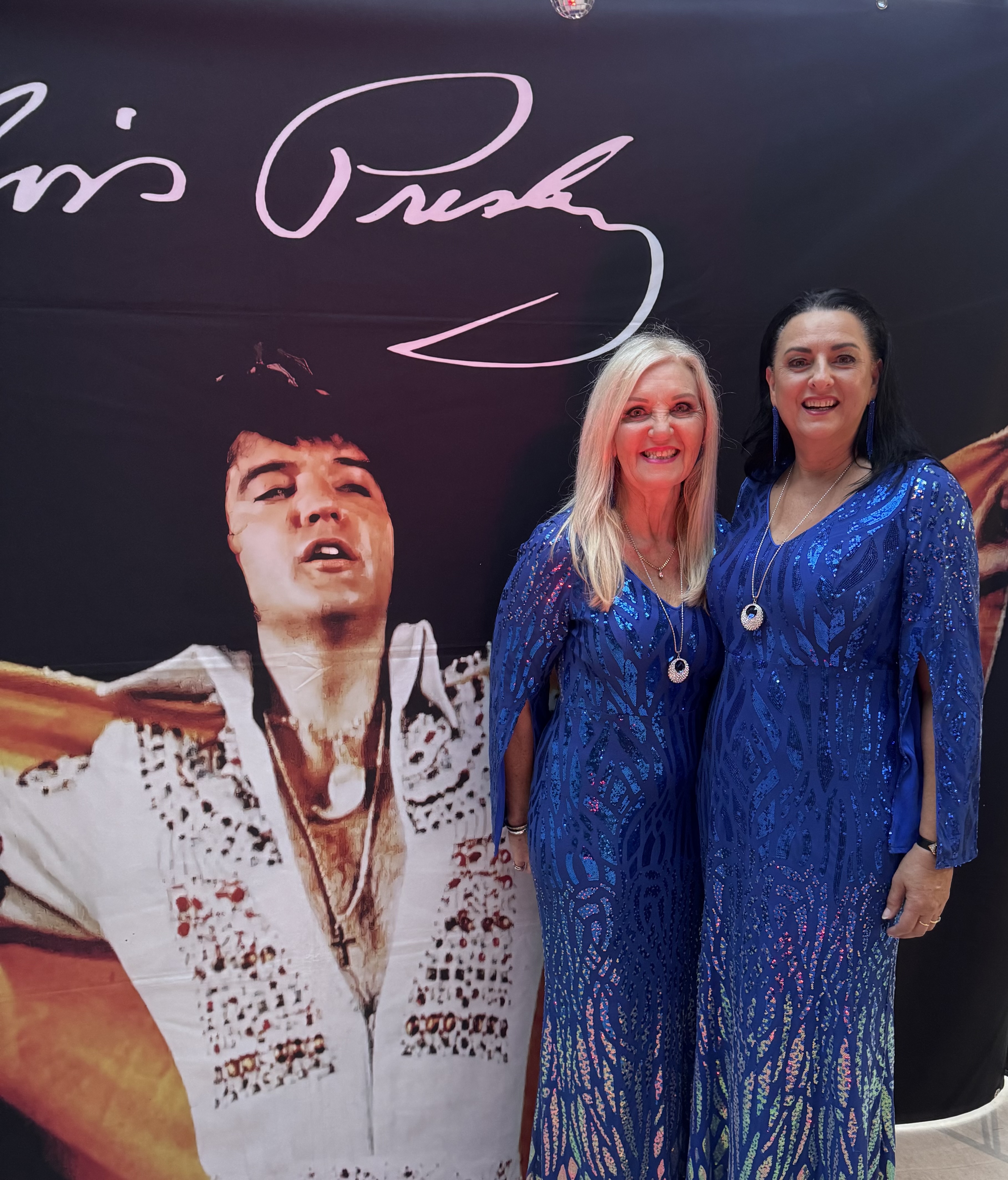 Jannine Douglas and Suzie in matching blue sequin gowns in front of the Elvis Presley backdrop
