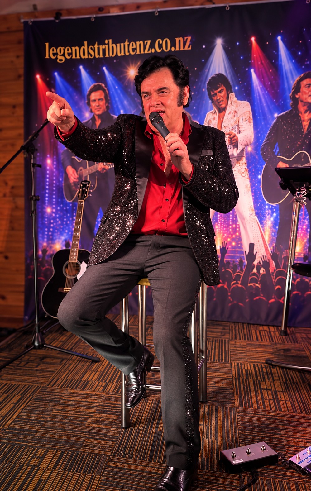 Trevor Needham as Neil Diamond pointing to the crowd while singing at Taupō Cosmopolitan Club with the legends banner